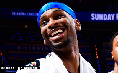 Smiling male boxer wearing a blue head wrap, robe on, in a boxing arena.